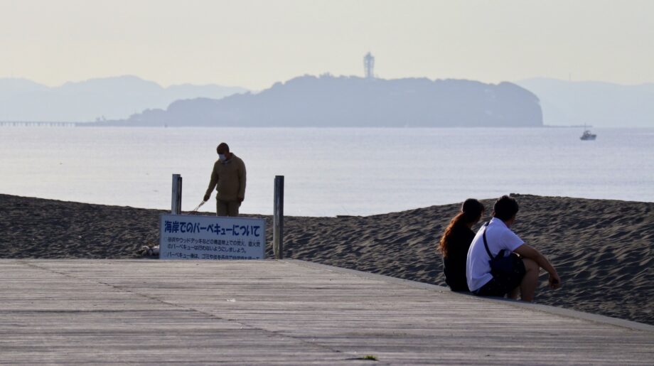 朝のボードウォークに腰掛ける人と遠くに見える江の島